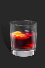 Studio-style photograph: low round glass with a classic Negroni cocktail of deep ruby-red color, garnished with a slice of orange. 