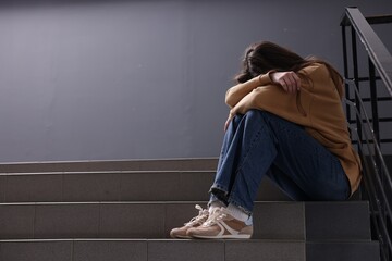 Bullying. Upset teenage girl on stairs indoors. Space for text