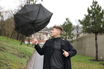 Man with broken umbrella fighting wind under rain outdoors