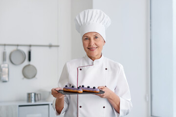 Smiling pastry chef holding tasty eclairs in kitchen
