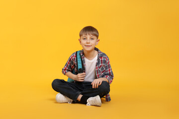 Cute schoolboy with backpack on orange background