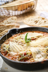 Shakshuka with baked eggs in tomato sauce, topped with melted cheese and basil, served hot in a...