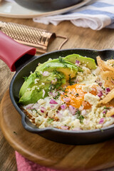 Fried egg with avocado, red onion, cheese, and crispy tortilla chips served in a cast iron skillet. Colorful and hearty breakfast close-up