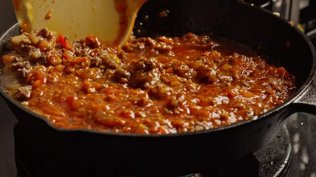 stirring hot and steaming bolognese sauce in pan, cooking bolonese sauce