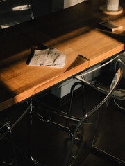 Sunlight illuminates a folded cloth tissue resting on a modern wooden table, with transparent...