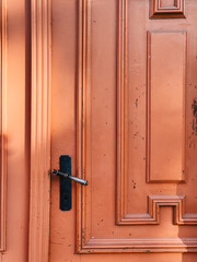 Sunlight illuminating old, weathered orange wooden door featuring classic metal handle and keyhole, showcasing texture and craftsmanship of a bygone era. Warm sunlight, weathered orange wooden door
