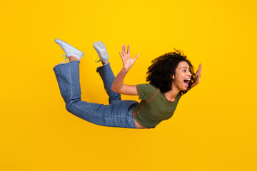 Energetic Young Woman Playfully Posing Midair in Casual Outfit Against a Vibrant Yellow Background