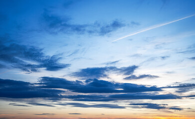 A tranquil evening sky with soft clouds and visible airplane contrails streaking across a gentle...