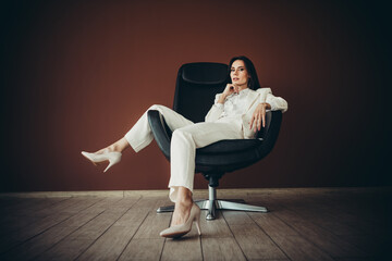 Beautiful businesswoman in an elegant white suit poses stylishly seated in a modern chair, exuding professionalism