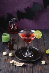 Red cocktail in martini glass in halloween theme decor on dark wooden background. Halloween celebration, party, themed drinks.