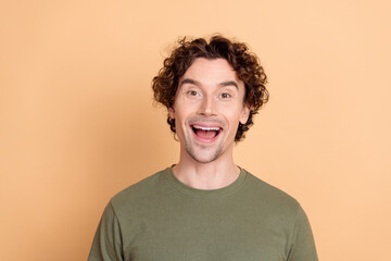 Young curly haired man in a casual khaki t-shirt expressing joy against a stylish beige background