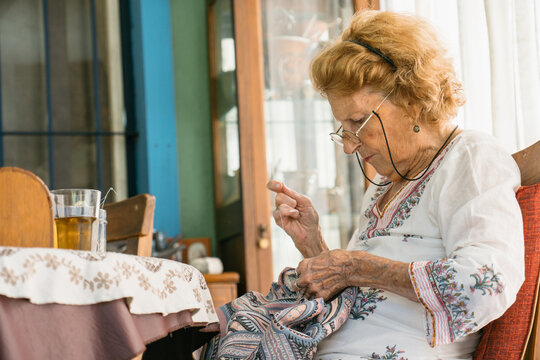 Elderly woman sewing by the table with herbal tea