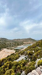 Vertical photo. A small airport runway stretches between hills on Kastellorizo Island, Greece. Remote island travel, Greek landscape, aviation, transportation, Mediterranean scenery, summer tourism. 