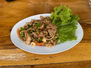 Spicy minced pork salad (Larb Moo), a popular Thai northeastern dish, served on a white plate with fresh vegetables on a wooden table.