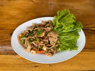 Spicy minced pork salad (Larb Moo), a popular Thai northeastern dish, served on a white plate with fresh vegetables on a wooden table.