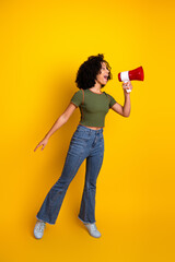 Stylish young woman with a megaphone on a vibrant yellow background expressing excitement and...