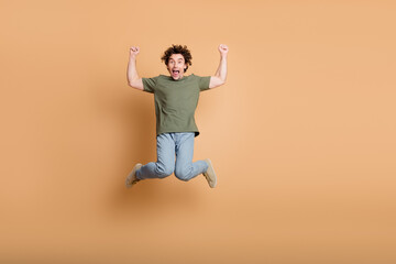 Joyful young man in casual attire jumping with excitement on a beige background, showcasing energy...