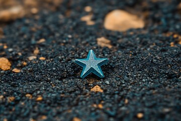 A small starfish lies on a dark beach with pebbles and sand around it, captured from a close-up viewpoint