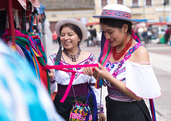 Two smiling indigenous women wearing traditional andean clothing and hats are choosing colorful...