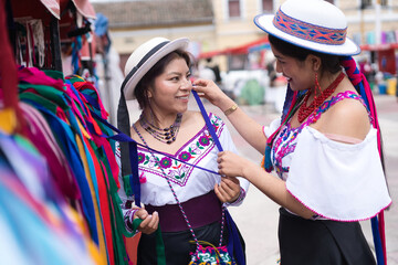 Indigenous women trying on traditional clothes at a colorful market stall