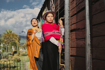 Two indigenous ecuadorian models are posing near an old wooden train, wearing colorful traditional...