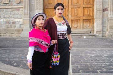 Two ecuadorian women wearing traditional andean clothing are posing together in front of a colonial...