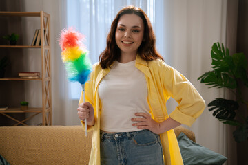 Young adult woman spending time at home, housekeeping time on weekend, woman in the living room dancing and cleaning dust from the table.