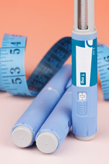 Blue measuring tape with semaglutide injection pens over red background