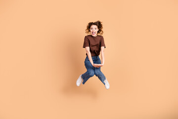 Cheerful Young woman energetically jumping with joy in casual attire against a beige background