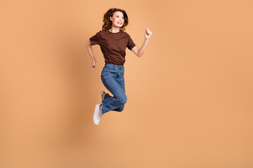 Cheerful female jumping joyfully in casual outfit against beige background showcasing stylish...