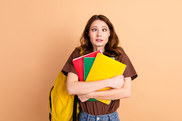 Confused young woman holding colorful notebooks against beige background, wearing casual brown...