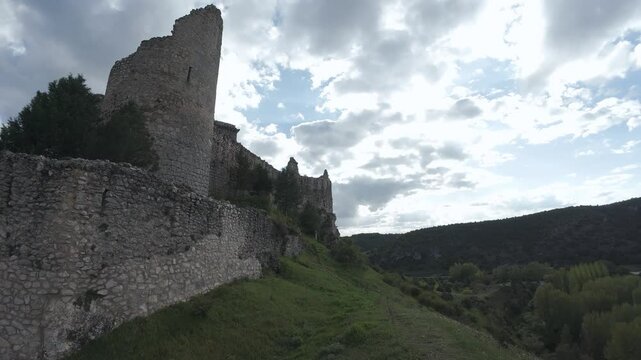 Medieval stone walls rising over green valley under cloudy sky