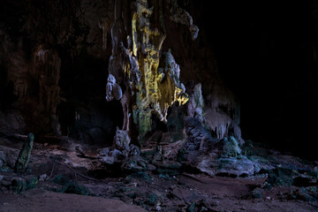 Mystical limestone cave chamber featuring illuminated stalactites, dramatic rock formations, and shadowy textures in a surreal underground landscape scene.