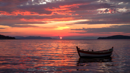 Fototapeta premium Stunning sunset over a calm lake with a solitary traditional wooden boat gently floating on the water, ideal for conveying peace and tranquility