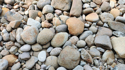 River rock background. A collection of river rocks with varying shapes, sizes and colors. Photo of rocks on the riverbank.