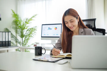 Professional businesswoman taking notes while working on laptop in modern office.