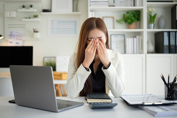 Young professional woman sitting at desk with hands on face, showing signs of burnout or...