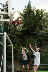 Fototapeta premium Young man and woman playing basketball on an outdoor court in a residential yard. Sunny summer day, green trees, clear blue sky. Active lifestyle and urban sport