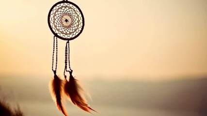 Close up of a dreamcatcher with feathers and beads hanging silhouetted against a golden sunset sky, bohemian style - Powered by Adobe