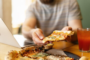 Freelancer enjoying pizza slice during work break in pizzeria