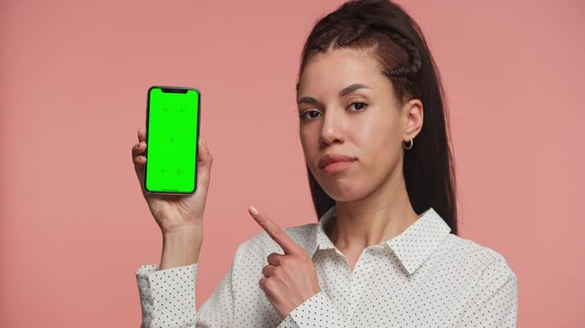 Woman pointing at smartphone with green screen on pink