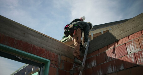 Construction workers descending ladder from rooftop, safety equipment in use, careful steps on...