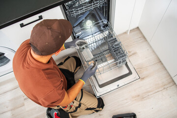 Technician Performs Maintenance on a Dishwasher in a Modern Kitchen During Daylight Hours With...