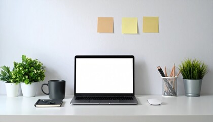 Minimalist workspace laptop with blank screen on white desk, plants, mug, & notes against a plain wall