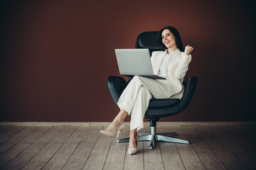 Beautiful businesswoman in white formalwear working on laptop while seated in a modern chair in a...
