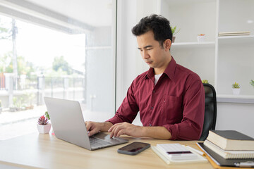 Fototapeta premium A man is typing on a laptop at a desk with a calculator, a notebook, and a stack of books. Concept of productivity and focus, as the man is working on a task that requires concentration 