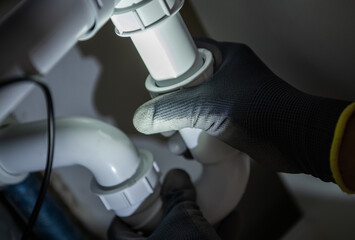 Plumber Repairing White PVC Pipes in a Residential Kitchen Under Sink During Evening Hours