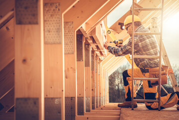 Construction Worker Using a Power Drill on a Wooden Frame in a Partially Built Structure During Sunset