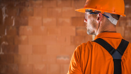 Construction Worker Wearing Safety Gear and Orange Uniform Assesses Building Progress at a Construction Site
