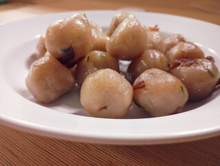 white plate is filled with glittering, round, light-colored cilok, some showing green flecks from their filling, against a warm wooden background.